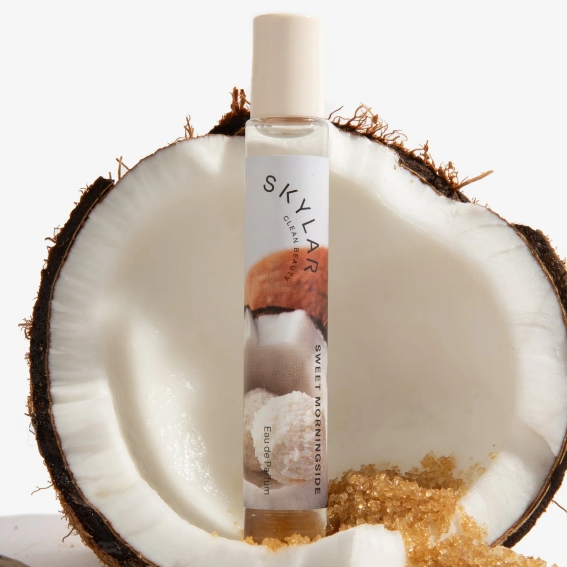 Photo of the Skylar Sweet Morningside rollerball perfume. Creamy white, located in a coconut with spilled brown sugar around it.