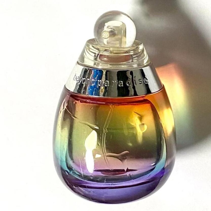 Photo of the Beyond Paradise perfume by Estée Lauder. Round, rainbow colored, semi-transparent bottle. Source: Portia Turbo.